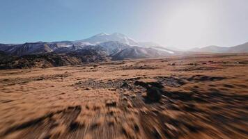 Low flight of a sports FPV drone at high speed high in the mountains over a yellow autumn field surrounded by snow-capped mountains of the Caucasus mountain range and Elbrus volcano video